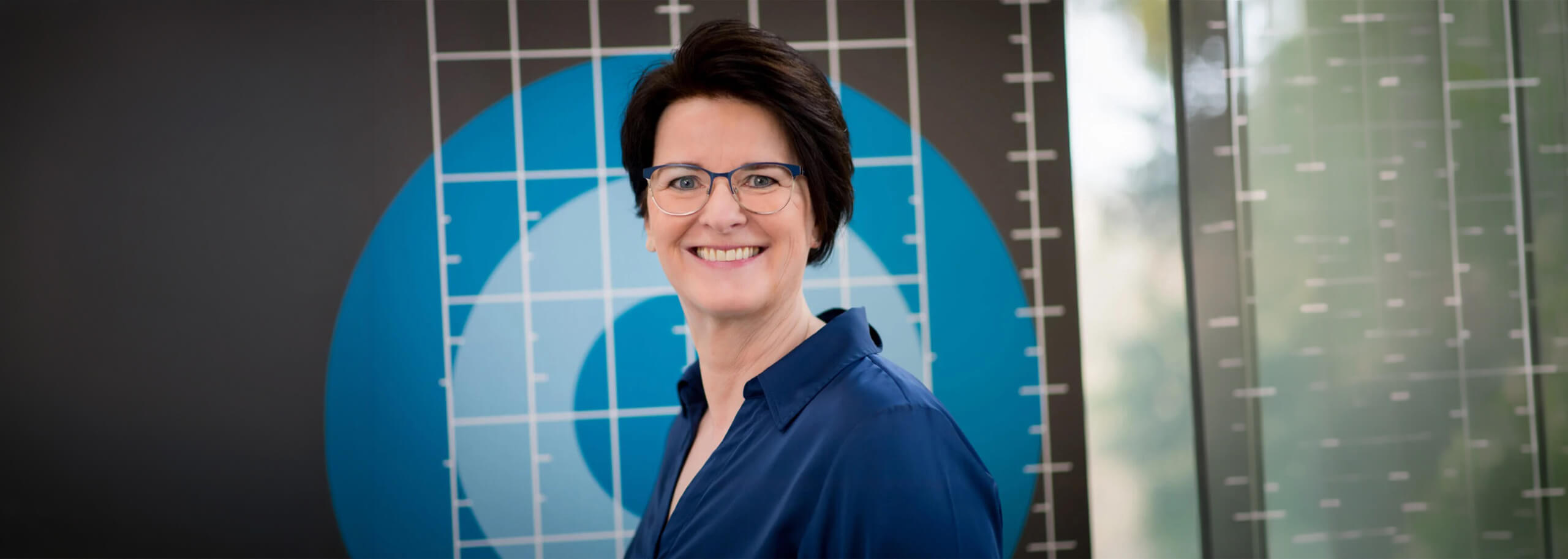 Frau mit Brille und kurzen dunklen Haaren lächelt.
